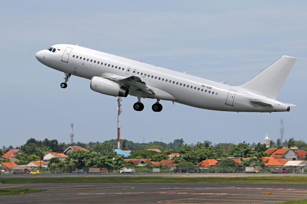 A commercial airplane lifts off from the runway, showcasing urban and rural backgrounds.
