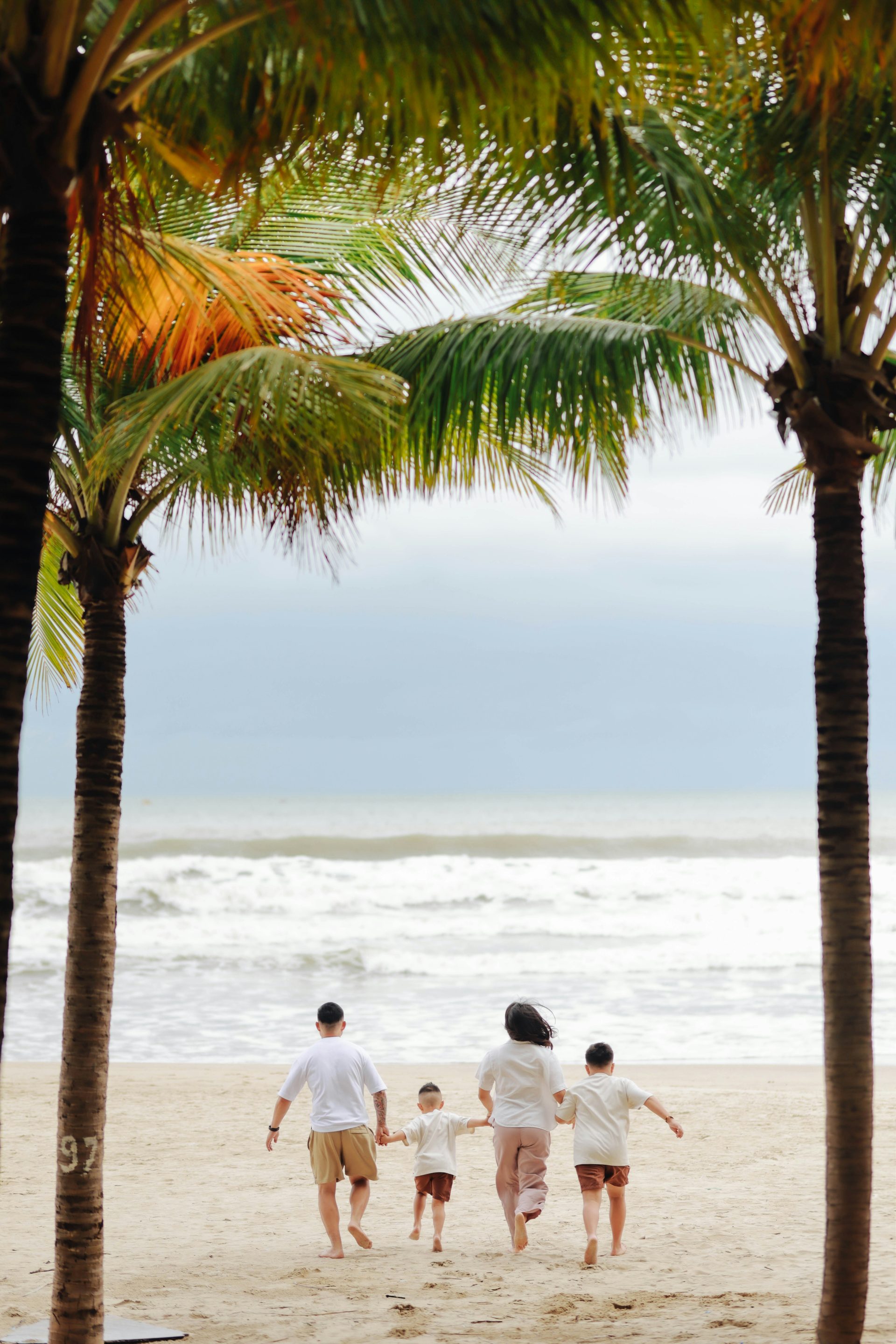 Family running towards the ocean through palm trees